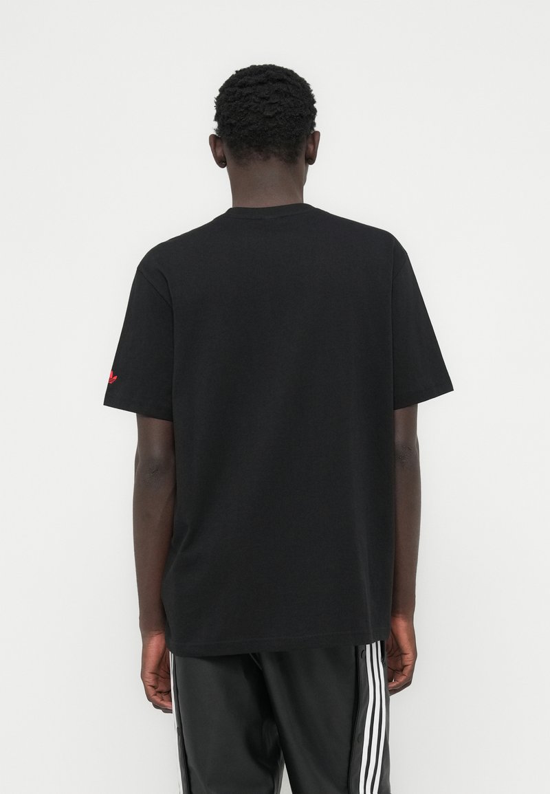 T-shirt en coton noir avec un col rond et des manches courtes, présentant un petit logo rouge sur la manche gauche. Design simple, coupe décontractée.