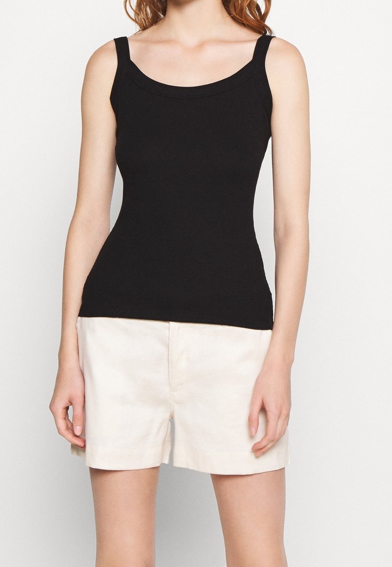 Czarny top na szerokich ramiączkach z dekoltem w serek, wykonany z miękkiego, elastycznego materiału. Połączony z jasnobeżowymi szortami o prostym kroju.