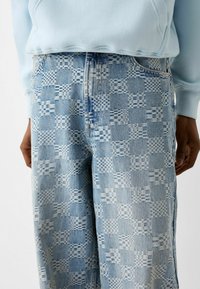 Jasnoniebieskie dżinsy w odcieniach niebieskiego z wzorem w szachownicę, luźny krój i widoczne detale szwów.