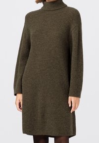 Robe tricotée vert olive avec un col roulé haut, des manches longues et une coupe décontractée, présentant une texture douce et atteignant mi-cuisse.