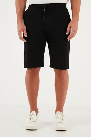 Zwarte katoenen shorts met een elastische tailleband en een trekkoord. Voorzien van zijzakken en een rechte snit, gecombineerd met witte sneakers.
