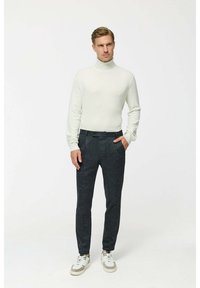 Weißer Rollkragenpullover kombiniert mit dunkel strukturierten Hosen und weißen Sneakern mit grauen Akzenten; lässige Passform, minimalistisches Design und neutrale Farben.