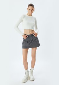 Valkoinen ribattu pitkähihainen crop-top, harmaa mini-hame, jossa on kaksi etutaskua, yhdistetty valkoisten alustassa lace-up-bootien ja harmaiden sukkien kanssa.