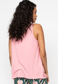 Jasnoróżowy top na ramiączkach o luźnym, swobodnym kroju, szerokich wycięciach na ramionach i miękkiej fakturze, uzupełniony wzorzystymi zielonymi spodniami z kwiatowymi printami.