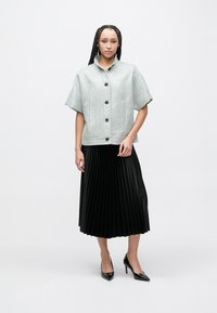 Tekstureret lysegrå kort jakke med korte ærmer og sorte knapper, kombineret med et sort plisseret midinederdel og sorte høje hæle.