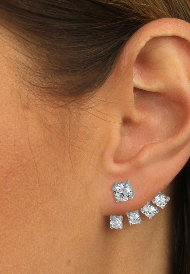 Oreille d'une femme avec une boucle d'oreille en argent courbé ornée de cinq pierres précieuses taillées en rond, disposées du plus petit au plus grand.