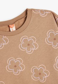 Tan trøje med rund hals, prydet med broderede pastelfarvede blomster i pink og lilla med brune midterdele på blødt, tekstureret stof.