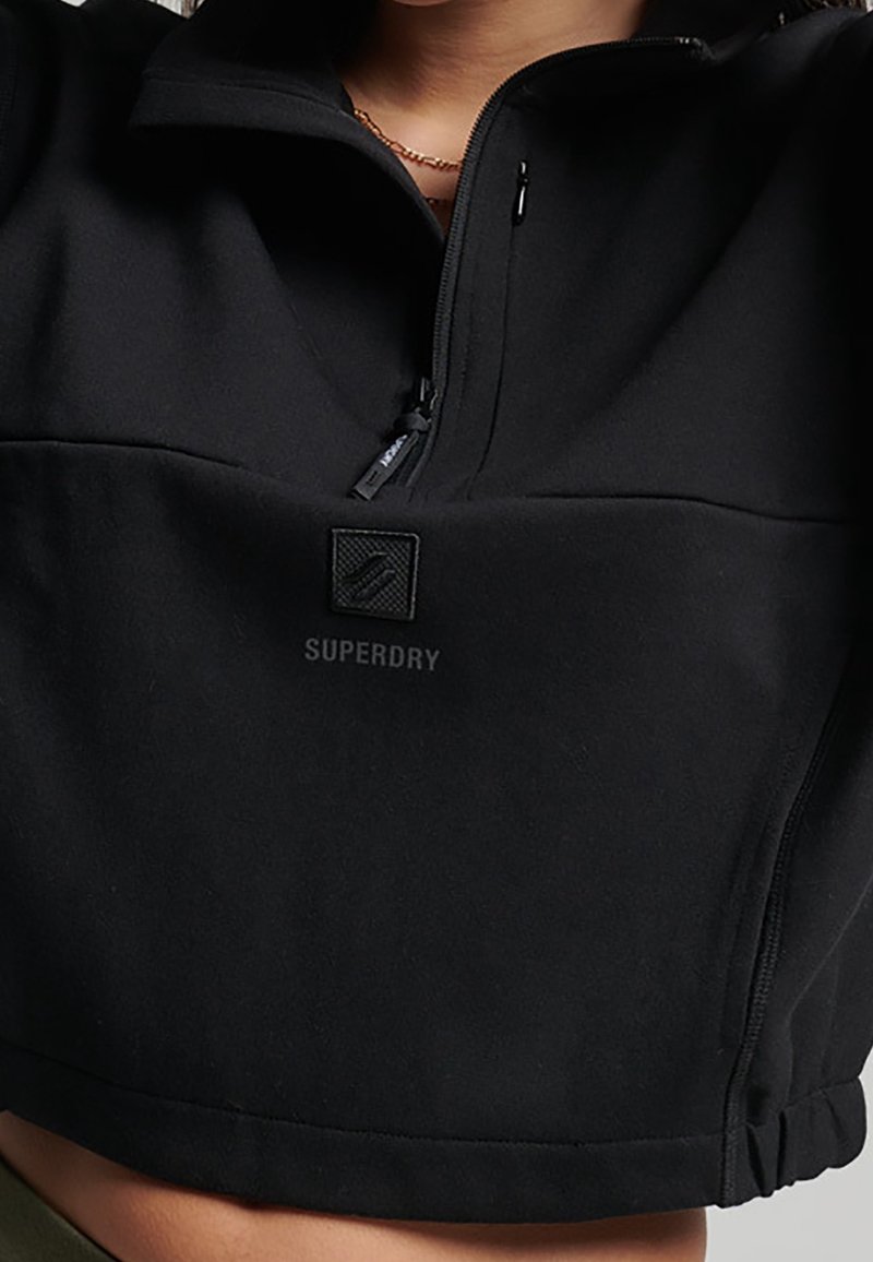 Pullover nero a maniche corte realizzato in tessuto morbido, con colletto alto, mezza cerniera e un piccolo logo patch sul davanti.