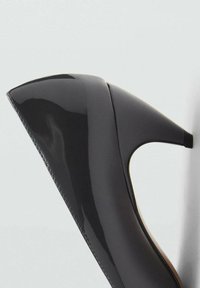Escarpin en cuir verni noir avec un bout pointu et une texture lisse, présentant une silhouette élégante et un design courbe.
