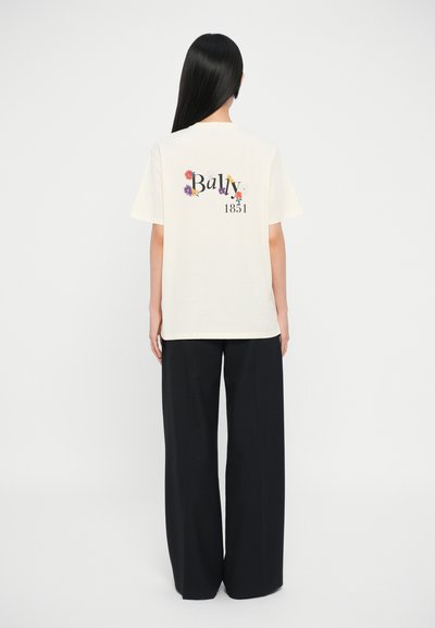 T-shirt en coton crème ornée de graphiques floraux colorés et du texte "Bally 1851" au dos. Associé à un pantalon large noir.