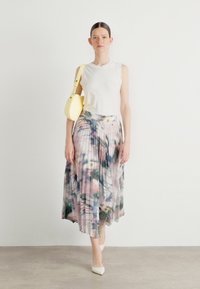 Top bianco senza maniche abbinato a una gonna plissettata con un motivo pastello. La modella porta una piccola borsa gialla e indossa tacchi bianchi.