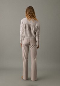 Light gray knitted sweater with fringe detail at the back, paired with light beige fitted pants. Smooth texture and casual design.