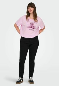 Pink cotton t-shirt with short sleeves and a graphic print of cowboy boots and text. Paired with black skinny jeans and black sneakers.
