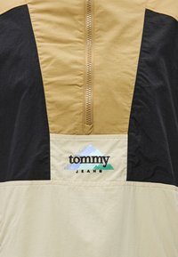 Ελαφρύ μπουφάν με φερμουάρ μέχρι το μέσο του στήθους, σε αποχρώσεις καφέ, μαύρου και κρεμ, με κεντημένο λογότυπο της μάρκας που απεικονίζει βουνό και λεία υφή.