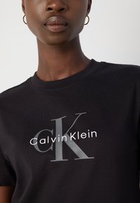T-shirt en coton noir avec un logo "CK" gris clair et le texte "Calvin Klein". Encolure ronde, manches courtes, texture lisse.