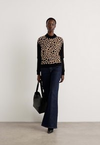 Svetr s leopardím vzorem v béžové a černé barvě, spárovaný s tmavými zvonovými džíny. Modelka nese černou koženou kabelku. Hladké textury všude kolem.