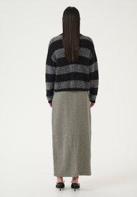 Black and gray striped knit sweater paired with a long, textured, gray skirt. The model wears black heeled shoes with bow accents.