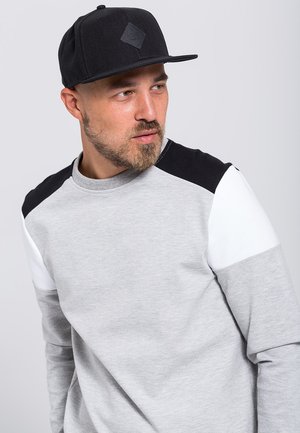 Pelēks sporta krekls ar melnbaltiem plecu akcentiem, apaļa dekoltē, garas piedurknes, kombinēts ar melnu plakano cepuri ar dimantu logotipu.