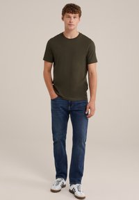 Tricou din bumbac de culoare verdeoliv, cu mâneci scurte, asociat cu blugi albaștri și adidași albi cu dungi negre. Design simplu și croială confortabilă.