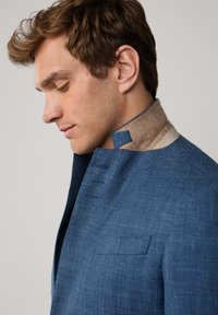 Modrá bunda s texturovanou látkou, která má jedinečný design límce v kontrastním tan materiálu a strukturované klopy.