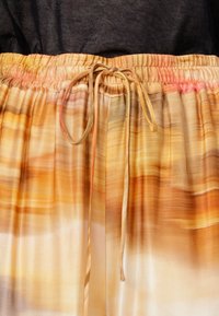 Elastisk midjeband med knytband; tyget har ett gradientmönster i varma färger av orange, gult och mjuk rosa, silkeslen textur.