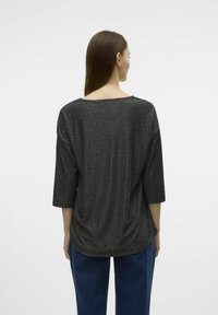 Top nero a coste con maniche a tre quarti, caratterizzato da un ampio scollo e un tessuto strutturato. Indossato su pantaloni blu, evidenziando una vestibilità comoda.