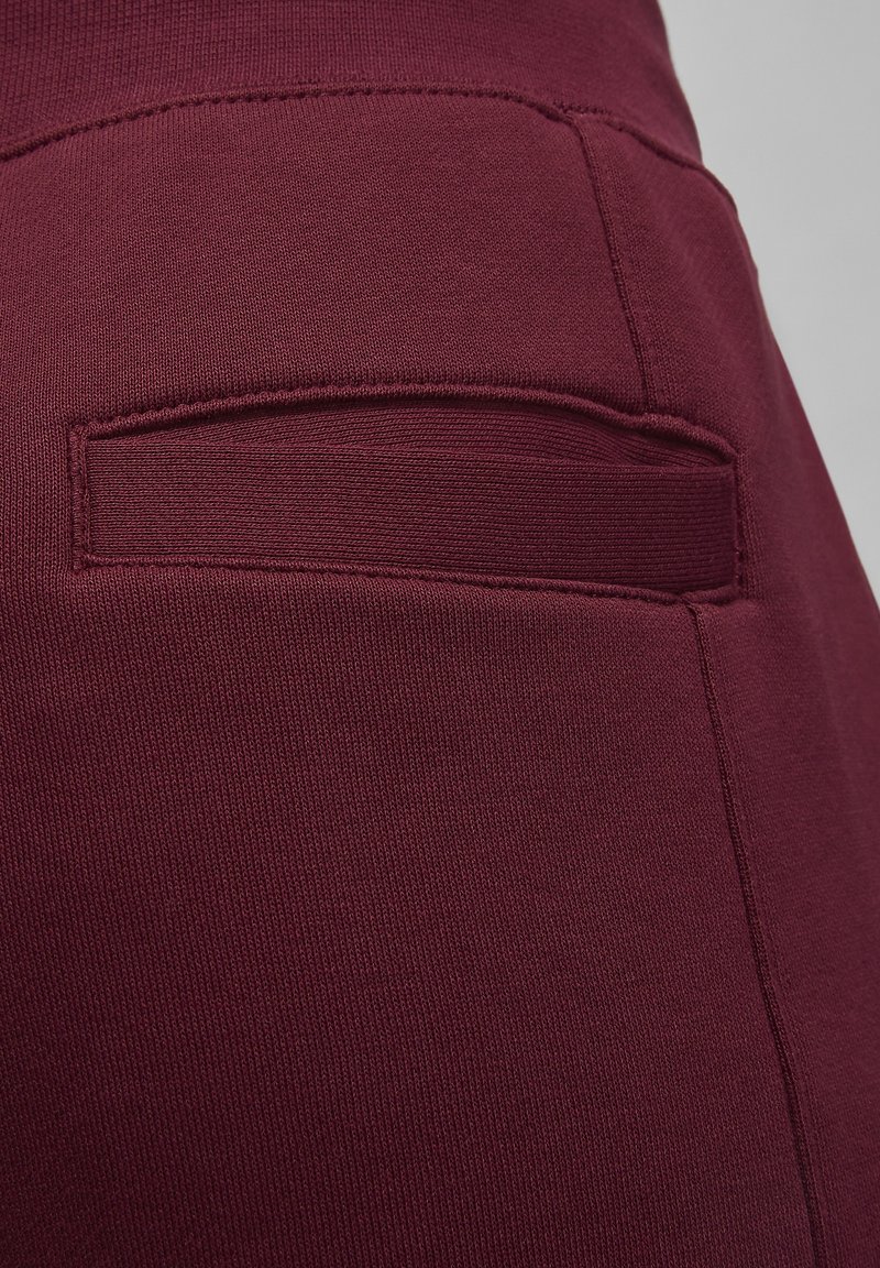 Burgunderfarbene Hose mit glatter Textur, einer genähten Gesäßtasche und einer taillierten Passform, hergestellt aus dehnbarem, bequemem Stoff.