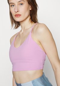 Sutiã desportivo rosa com um design em V e alças finas. Feito de tecido suave, apresenta um comprimento curto e detalhes discretos de costura.