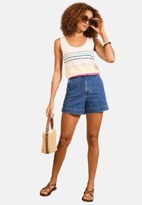 Tank top in light gray with multicolored stripes, paired with high-waisted denim shorts. Model holds a woven bag and wears sunglasses.