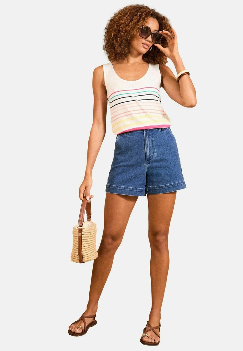 Tank top in light gray with multicolored stripes, paired with high-waisted denim shorts. Model holds a woven bag and wears sunglasses.