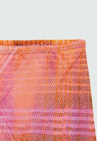 Tissu à motifs dans des teintes d'orange et de rose avec un motif en tartan. Présente une texture lisse et un bord stitché. Orientation horizontale.