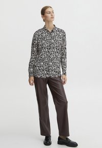 Long-sleeve button-up shirt with a black and white abstract pattern, paired with glossy brown faux-leather trousers and black loafers.