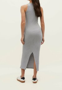 Robe longue en jersey gris à la coupe ajustée, sans manches, avec une fente latérale. Portée avec des baskets blanches ornées d'un accent noir.