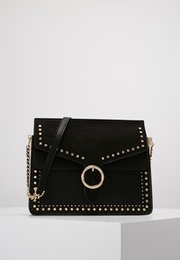 Borsa a tracolla in suede nero con forma strutturata, accessori in tonalità oro, dettagli a borchie e un anello decorativo sul davanti. Dotata di una tracolla a catena.