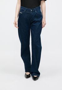 Tamsiai mėlynos spalvos džinsai iš džinso audinio, laisvo silueto, su penkiomis kišenėmis ir sidabrinio mygtuko užsegimu. Lygus paviršius su minimaliais dekoratyviniais elementais.