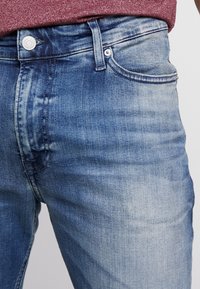 Hellblaue Denim-Jeans mit einer ausgewaschenen Textur, Fünf-Taschen-Design und einem silbernen Knopfverschluss an der Taille.