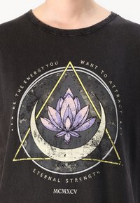 Svart t-shirt med en grafisk design som inkluderar en lila lotusblomma och geometriska former, inklusive en triangel och en halvmåne, med textaccenter.
