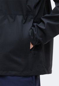 Άτομο που φοράει μαύρο μπουφάν με το δεξί χέρι στην πλαϊνή τσέπη, δείχνοντας τις λεπτομέρειες του μανικιού και της τσέπης.