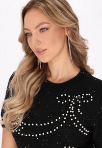 Czarny dzianinowy sweter ozdobiony rozsianymi białymi perłami i czarnym detalem w postaci kokardy. Miękka tekstura, krótkie rękawy i okrągły dekolt.