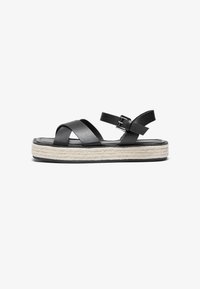 Sorte svarte lær platå sandaler med kryssende stropper, justerbar ankelspenne og en jute-innpakket såle. Flat gummisåle for grep.