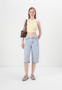 Top court rayé jaune, pantalon capri en denim bleu clair avec broderies florales, sac à bandoulière marron, baskets grises. Tenue simple et décontractée.