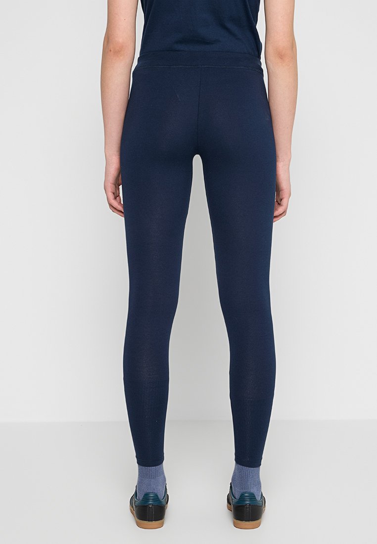 Leggings elasticizzati blu navy con un design elegante. Presentano una vita elastica e una texture liscia. Indossati con scarpe scure e calzini chiari.
