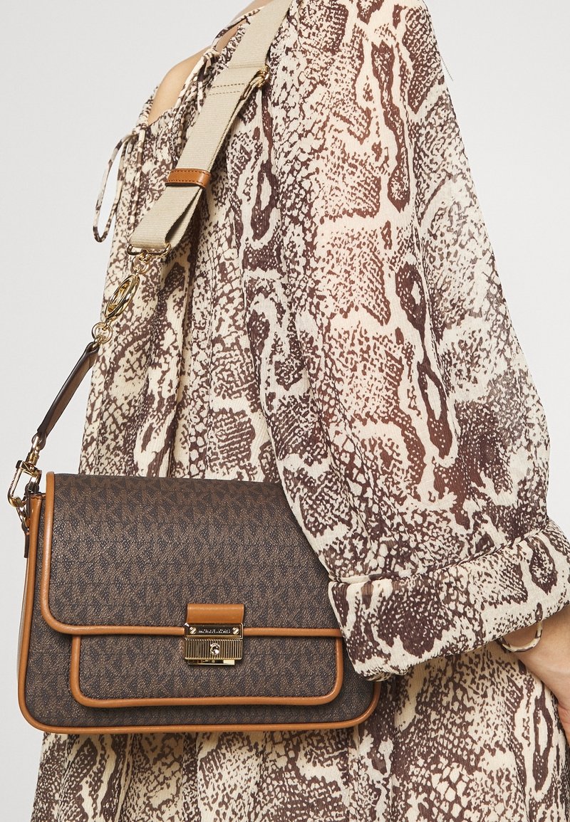 Sac bandoulière marron à motif avec garniture en cuir couleur noisette et fermoir doré porté sur l'épaule, associé à une robe à manches longues imprimé peau de serpent.