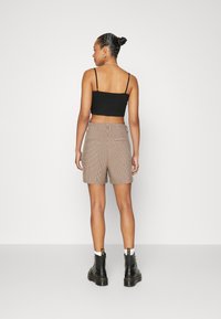 Shorts à carreaux marron avec poches latérales, taille élastique, et un top court noir. Des bottes noires à lacets complètent la tenue.