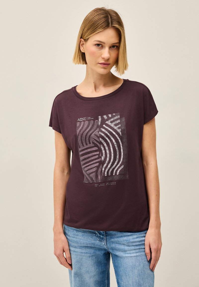 Mørkerød t-shirt med afslappet pasform, rund halsudskæring og korte ærmer. Forsiden prydes af et hvidt grafikdesign med bølgede linjer og tekst.