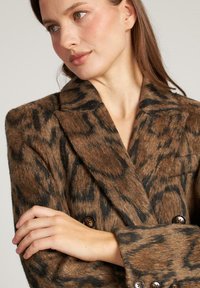 Bruine dubbelgeknoopte blazer van een zachte, gestructureerde stof met een zwart dierenprint, reverskraag en bruine knopenaccenten.