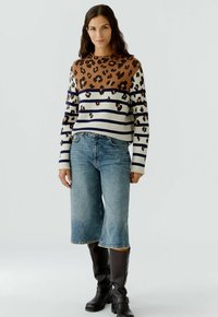 Pull rayé marron et crème avec un motif léopard, associé à un jean bleu clair à jambes larges et des bottes marron foncé jusqu'au genou.