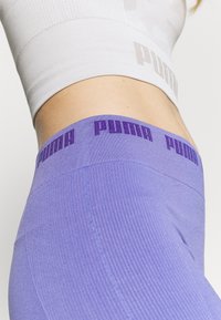 Puma-markierte lila Leggings haben eine gerippte Textur und einen breiten Bund mit wiederholtem Logo. Das Material ist dehnbar und enganliegend.