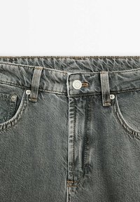 Jeans en denim gris avec une fermeture à boutons, présentant des coutures beige contrastantes et un design classique à cinq poches. Texture douce et aspect usé.