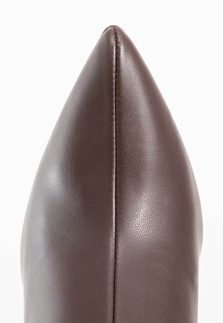 Chaussure en cuir marron à bout pointu avec une texture lisse, présentant une couture centrale et une silhouette élégante. Aucun ornement ni accent visible.